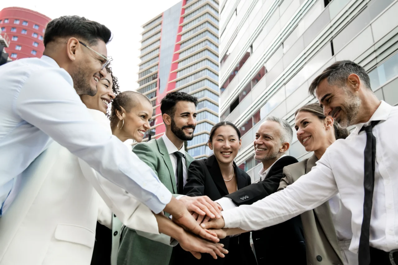 A group of employees in formal attire join hands.