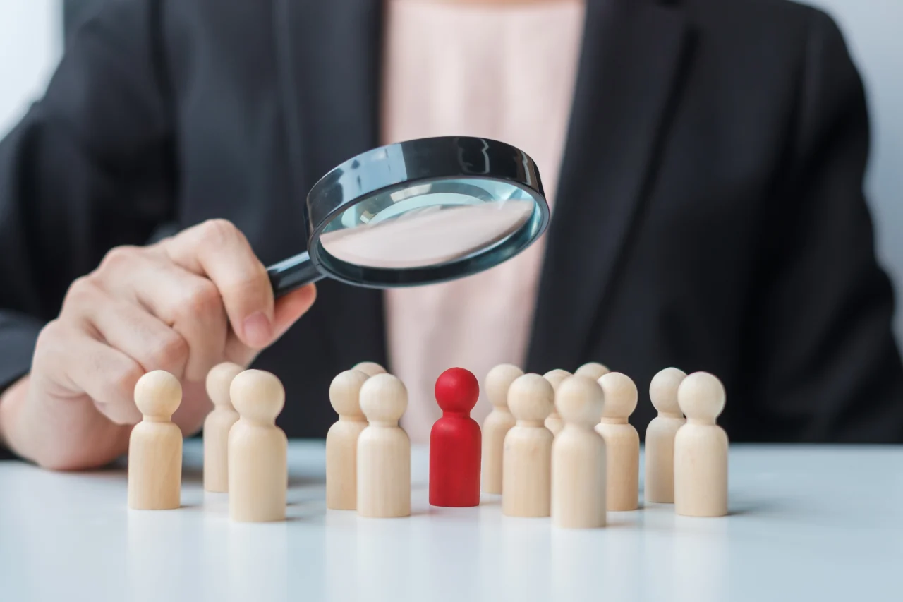 Employee investigation involving a person holding a magnifying glass on employee-shaped figurines on table.
